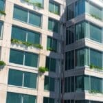 Edificio moderno con paneles solares rodeado de vegetación verde, en un entorno urbano sostenible.