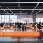 Espacio de coworking moderno con emprendedores trabajando en proyectos tecnológicos, mesas de trabajo y dispositivos electrónicos en uso por la tarde.