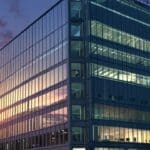 Edificio moderno de oficinas al anochecer con luces encendidas reflejando tecnología avanzada.