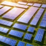 Imagen aérea de un parque fotovoltaico extenso al atardecer con paneles solares alineados.